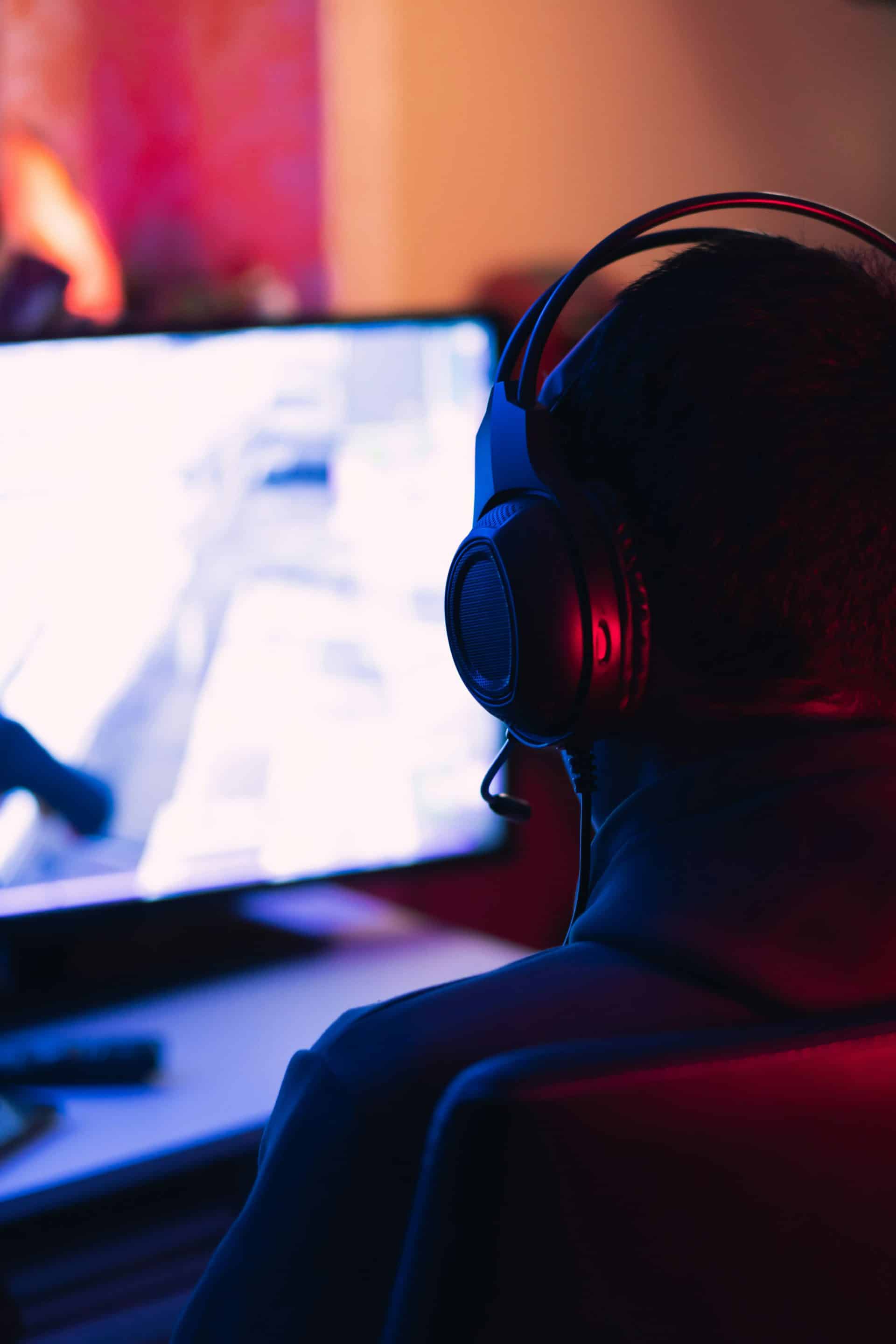 Gamer sitting at the monitor playing a video game with a gamer headset on.